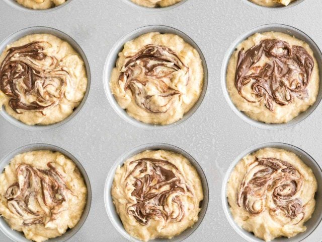 Vue d'en haut d'un moule à muffins gris avec une pâte à muffins banane nutella à l'intérieur avant la cuisson.