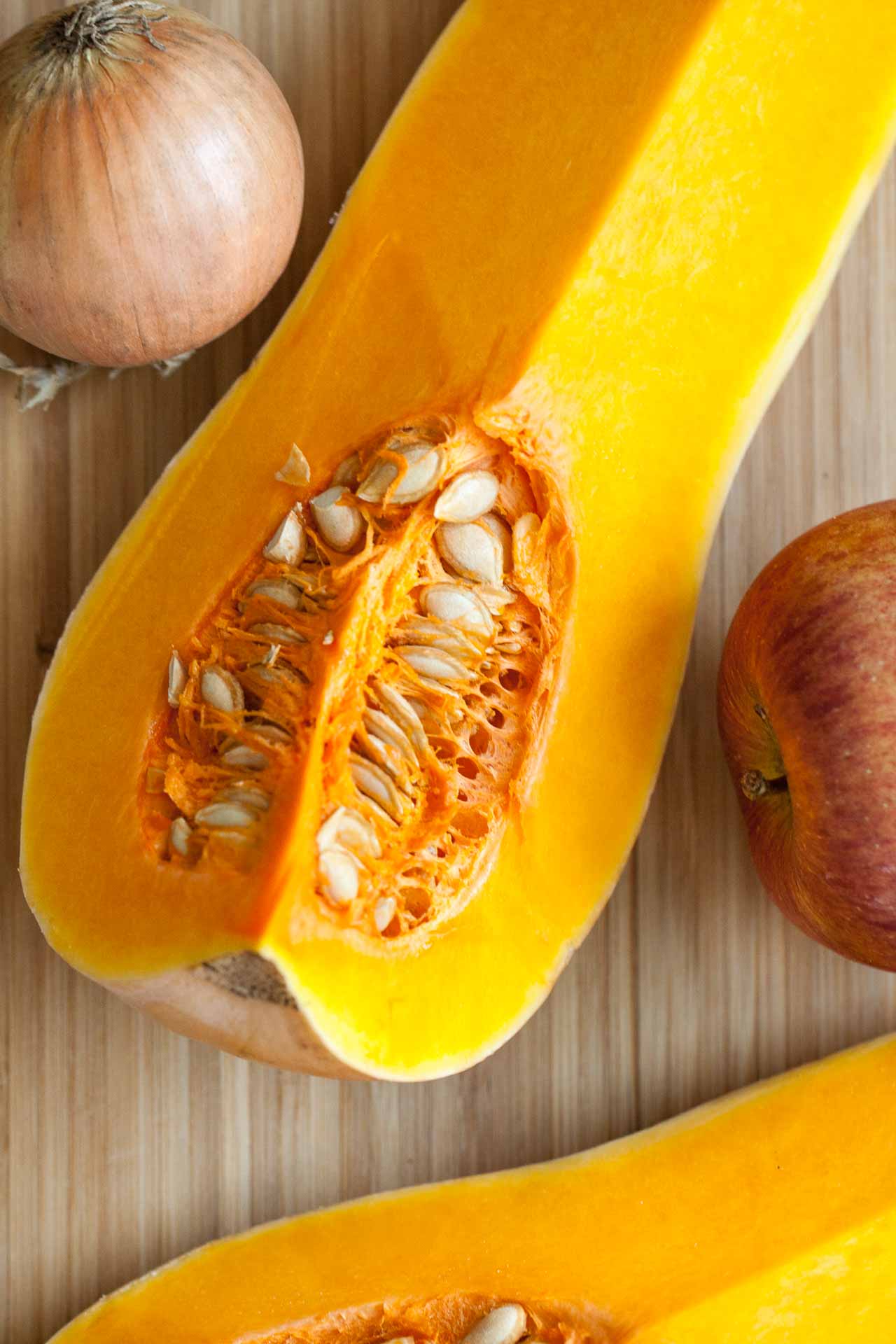 Vue du dessus d'un quart de potiron butternut, d'un oignon et d'une pomme sur une planche à découper en bambou.