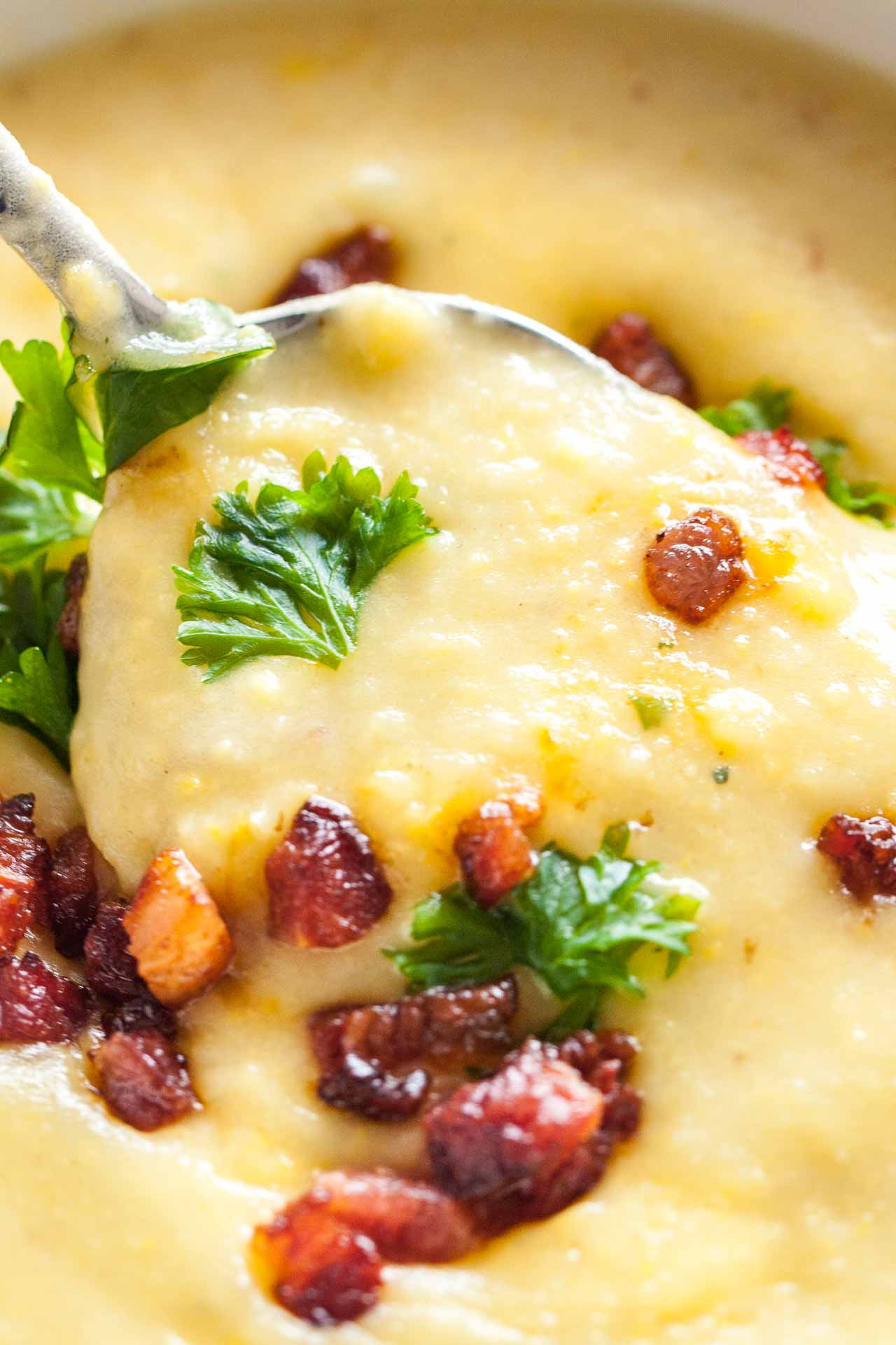 Gros plan d'une cuillère soulevant une portion de soupe de pommes de terre garnie de bacon et de persil.