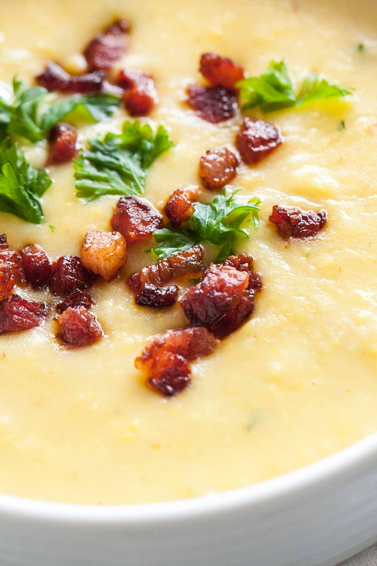 Gros plan d'un bol blanc de soupe de pommes de terre garni de bacon et de persil avec une cuillère dedans.