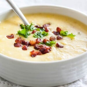 Un bol blanc de soupe de pommes de terre garni de bacon et de persil avec une cuillère dedans sur une nappe blanche.