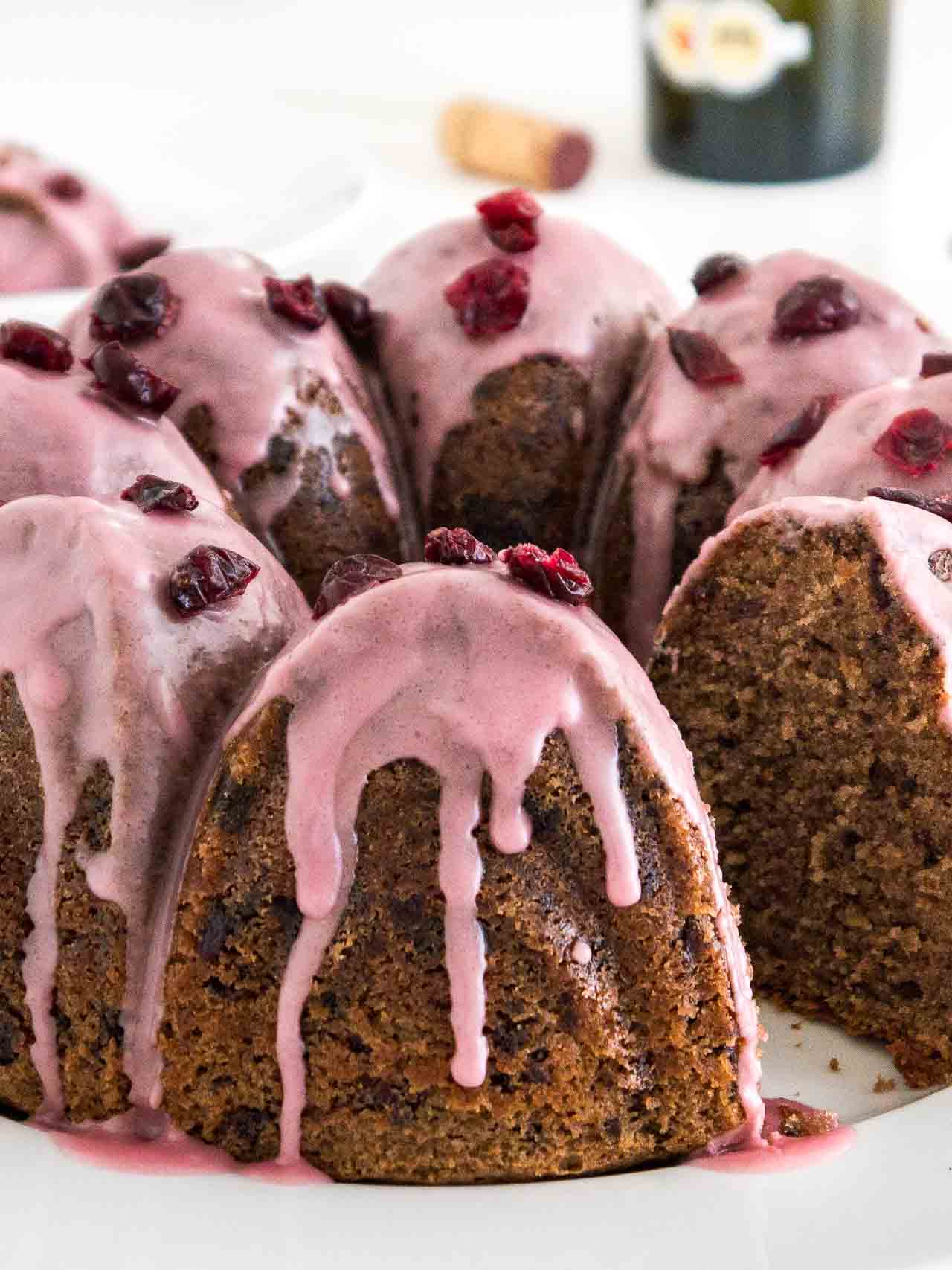 Gros plan sur un gâteau bundt au chocolat et aux canneberges avec un glaçage rose, garni de canneberges séchées sur une assiette blanche. Un morceau du gâteau a été découpé.