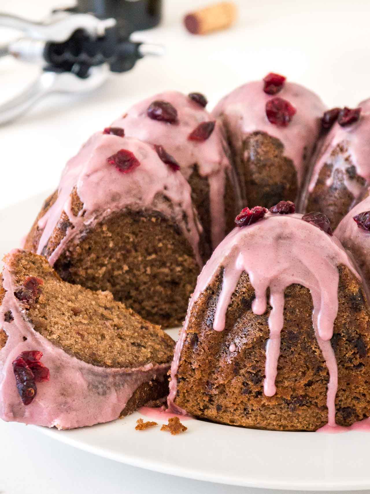 Gâteau bundt au chocolat et aux canneberges avec un glaçage rose, garni de canneberges séchées sur une assiette blanche. Un morceau du gâteau a été découpé et se trouve devant.