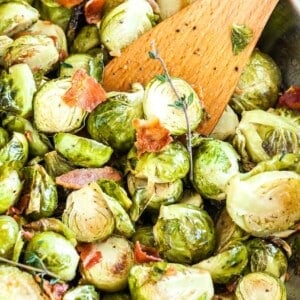 Choux de Bruxelles rôtis avec du bacon et une branche de thym dans une poêle en acier inoxydable.