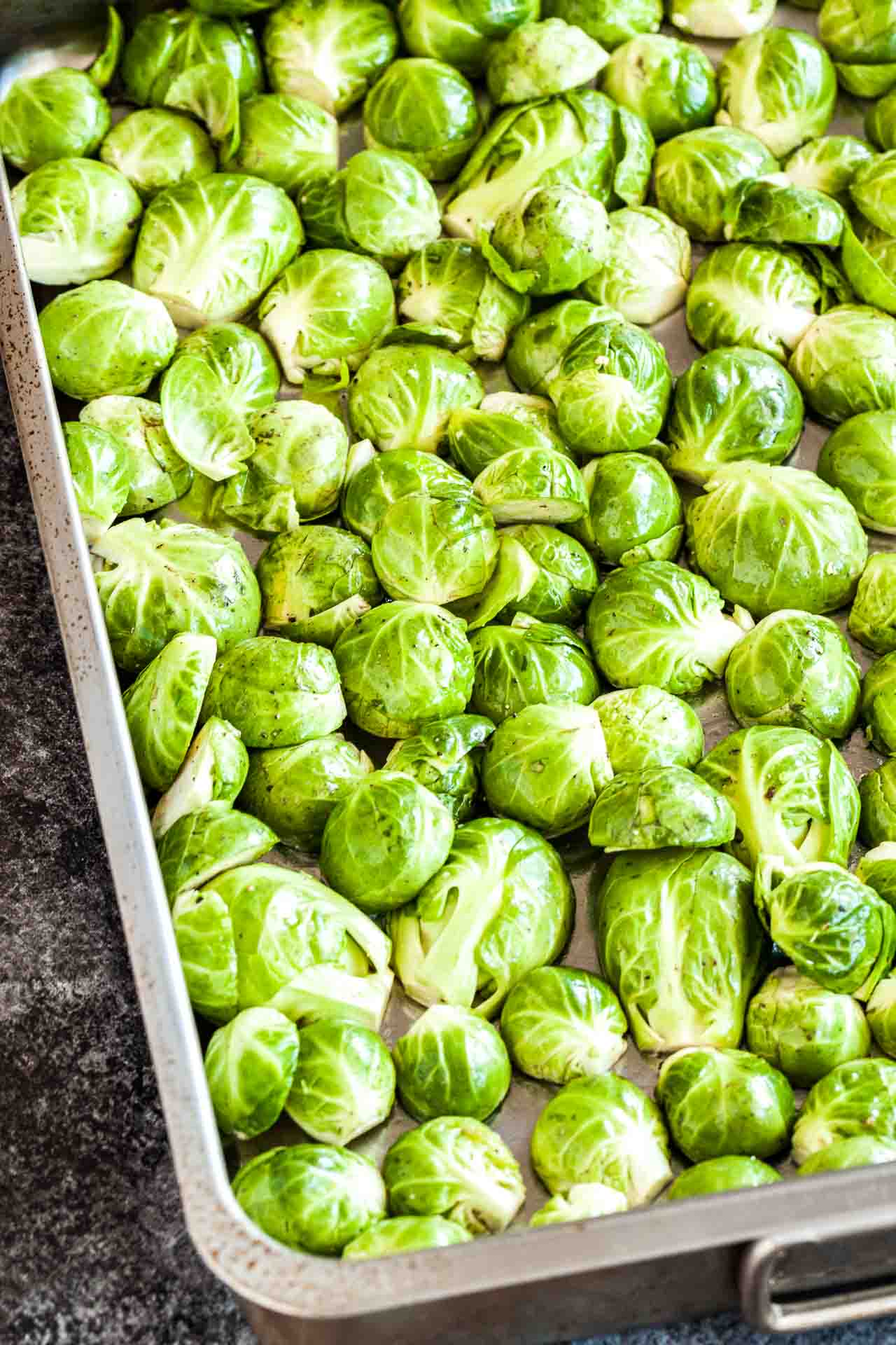 Choux de Bruxelles crus coupés en deux, couverts d'huile, de sel et de poivre sur une plaque de cuisson.