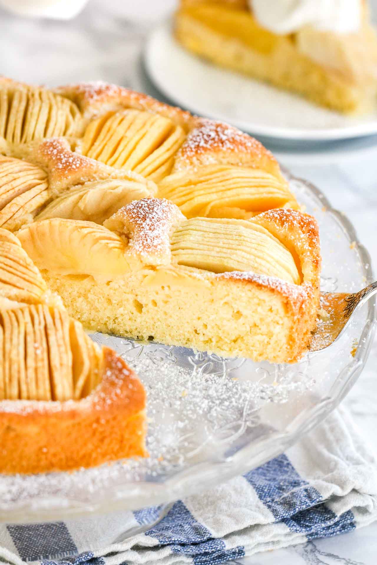 Un gâteau avec des pommes coupées en quartiers enfoncées dans le dessus, sur un plateau en verre.