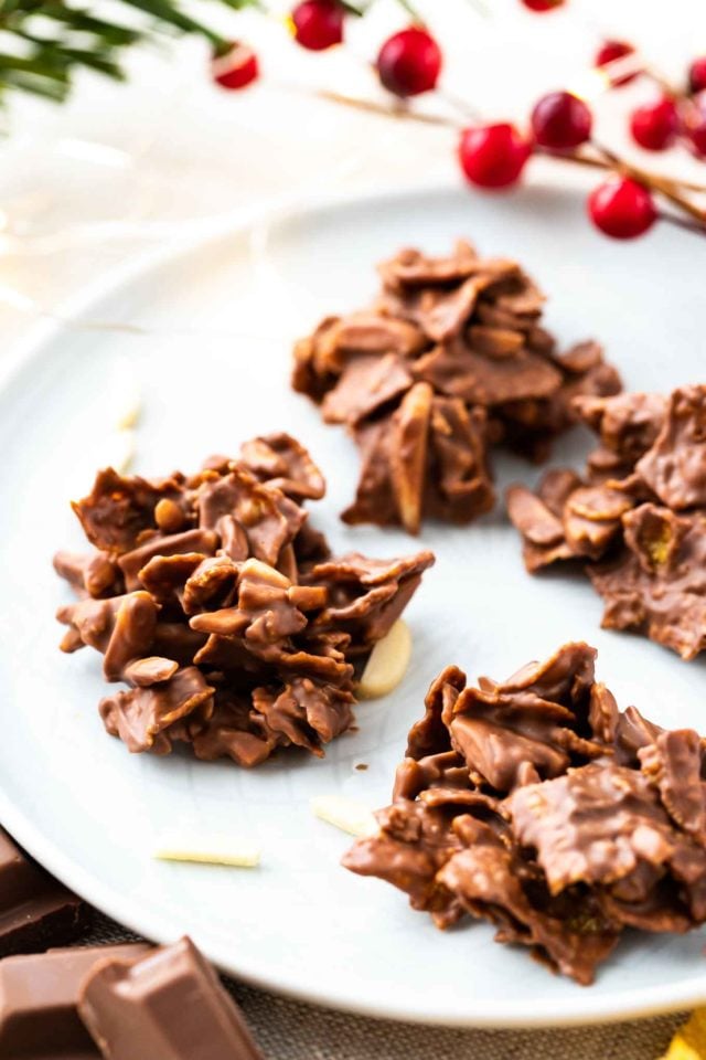 clusters de corn flakes et d'amandes enrobés de chocolat sur une assiette grise, garnis d'amandes et de cranberries