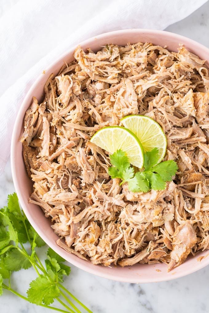Carnitas au mijoteur dans un bol rose garnies de quartiers de lime et de coriandre
