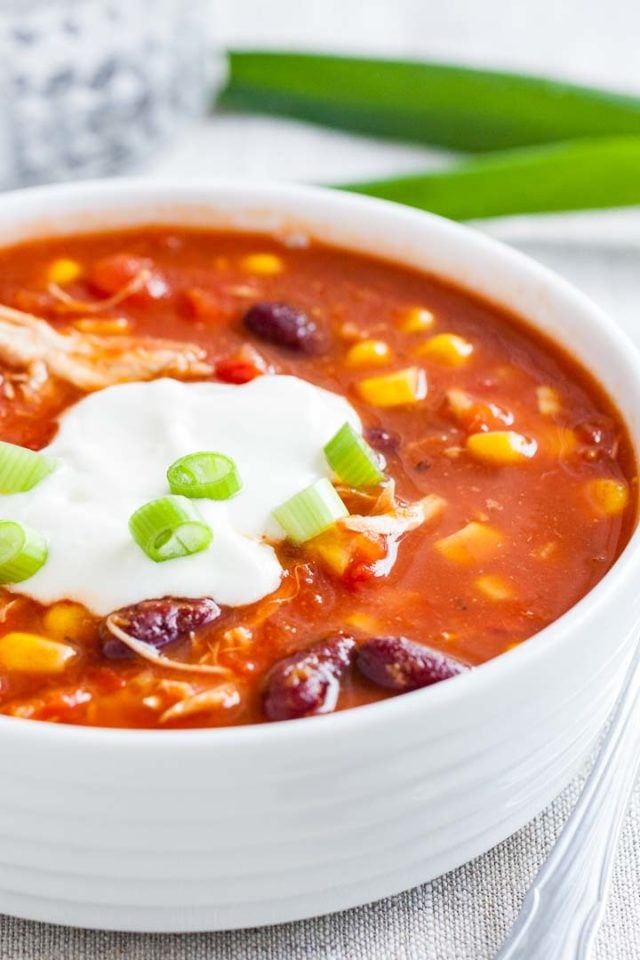 Gros plan d'un bol blanc de chili au poulet, garni de crème aigre et de ciboulette.