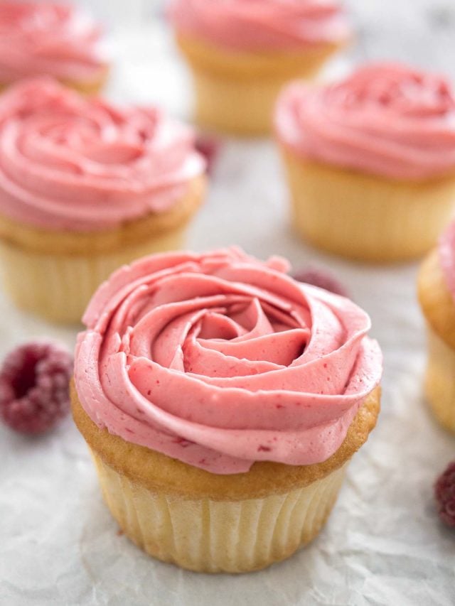 Cupcakes au citron et framboise avec glaçage framboise rose à côté de quelques framboises.
