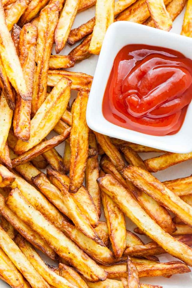 Vue de dessus de frites croustillantes avec un petit bol rectangulaire blanc de ketchup.