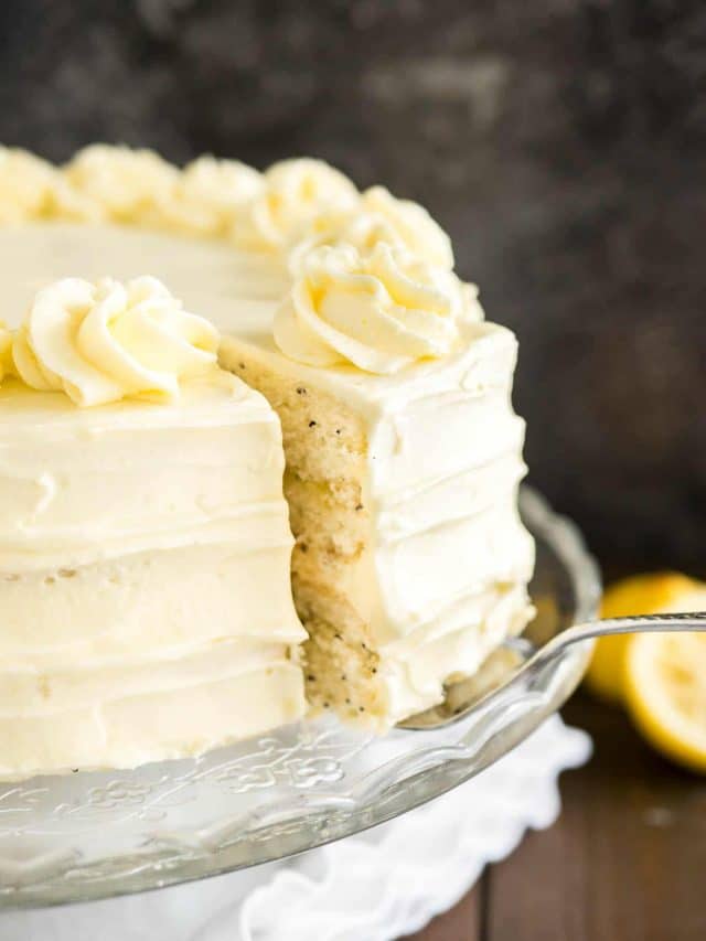 Gros plan d'un plat en verre avec un gâteau au citron et aux graines de pavot sur une table en bois avec une nappe blanche. Un serveur à gâteau soulève une part.
