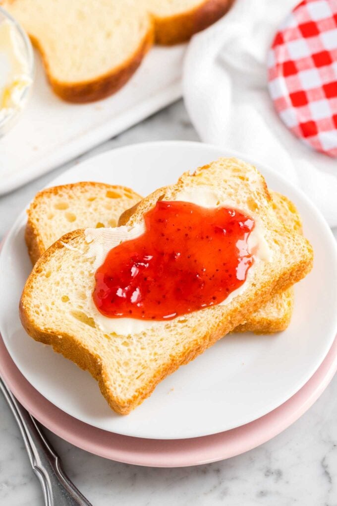 Deux tranches de pain sur une assiette avec du beurre et de la confiture étalés dessus