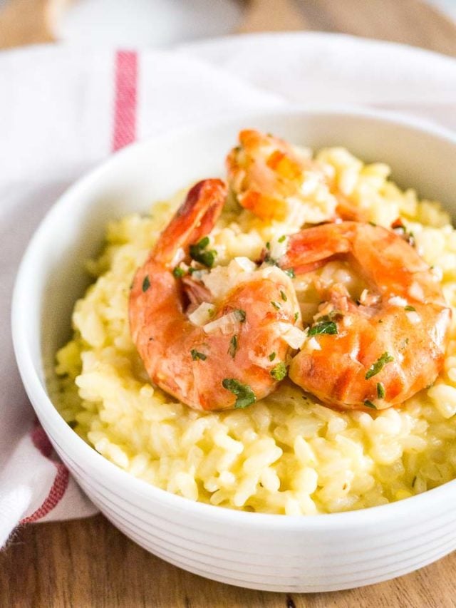 Gros plan d'un bol blanc avec du risotto au safran et des crevettes frites sur un torchon de cuisine blanc avec une rayure rouge.