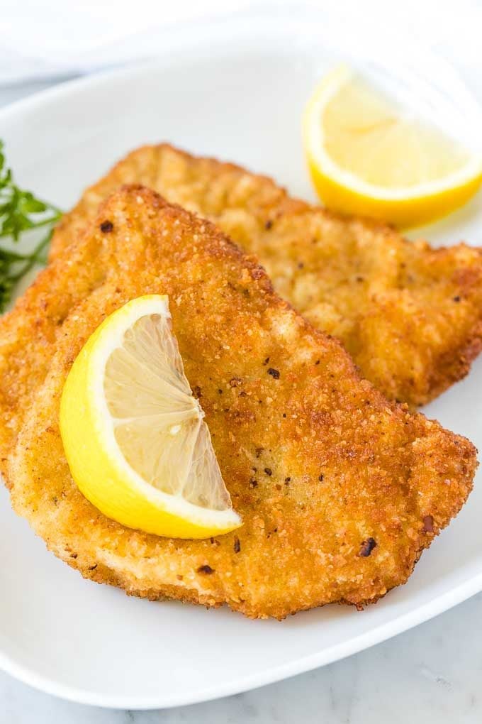 Deux escalopes frites sur une assiette blanche, garnies d'un quartier de citron et de persil