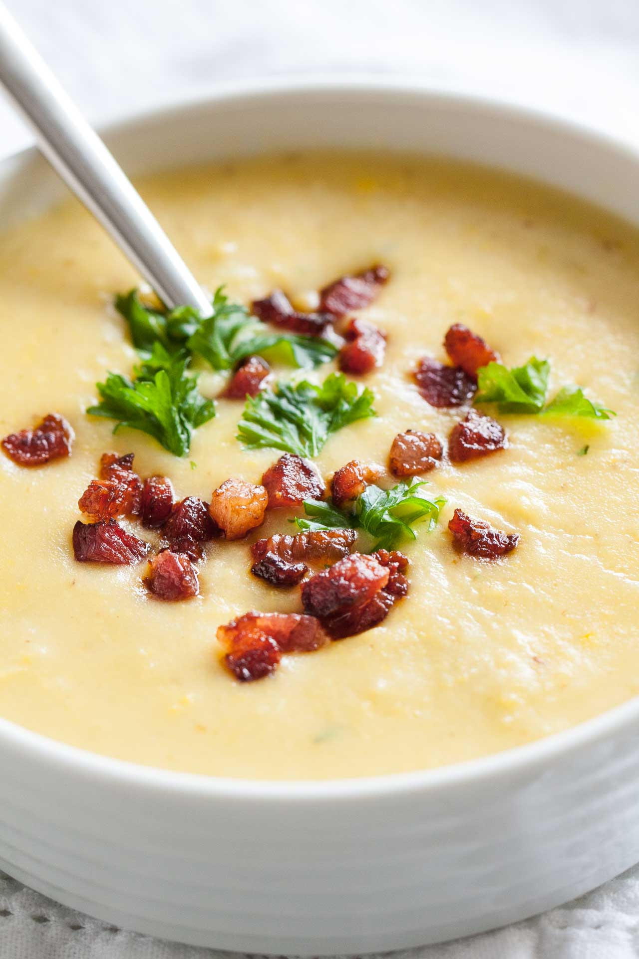 Gros plan d'un bol blanc de soupe de pommes de terre garni de bacon et de persil avec une cuillère dedans.
