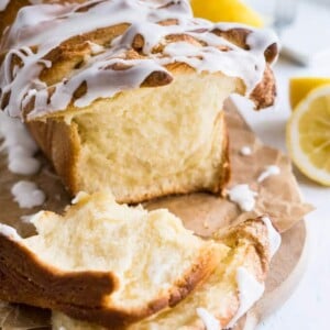 Un pain à séparer au citron avec un glaçage au citron sur un morceau de papier brun sur une planche à découper en bois à côté de quelques citrons coupés en deux.