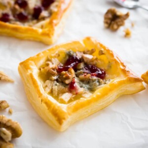 Mini-tartes aux poires et au gorgonzola avec sauce aux canneberges sur du papier sulfurisé, garni de noix, avec une cuillère à côté.