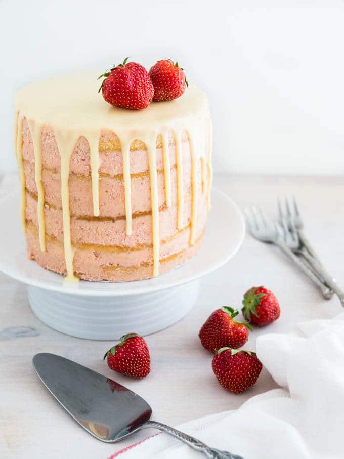 Le Naked Strawberry Layer Cake est réalisé avec une crème au beurre meringuée à la fraise fraîche et des couches de gâteau à la vanille aériennes. Terminé par un coulis de ganache chocolat blanc sur les bords, ce gâteau est une magnifique pièce maîtresse pour chaque occasion spéciale !
